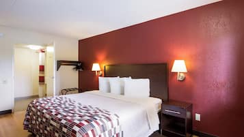 A hotel room with a bed, a nightstand, a lamp, and a door leading to a bathroom.