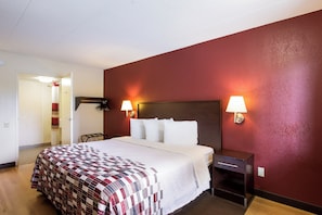 Une chambre d’hôtel comprenant un lit, une table de chevet, une lampe et une porte donnant sur une salle de bain.