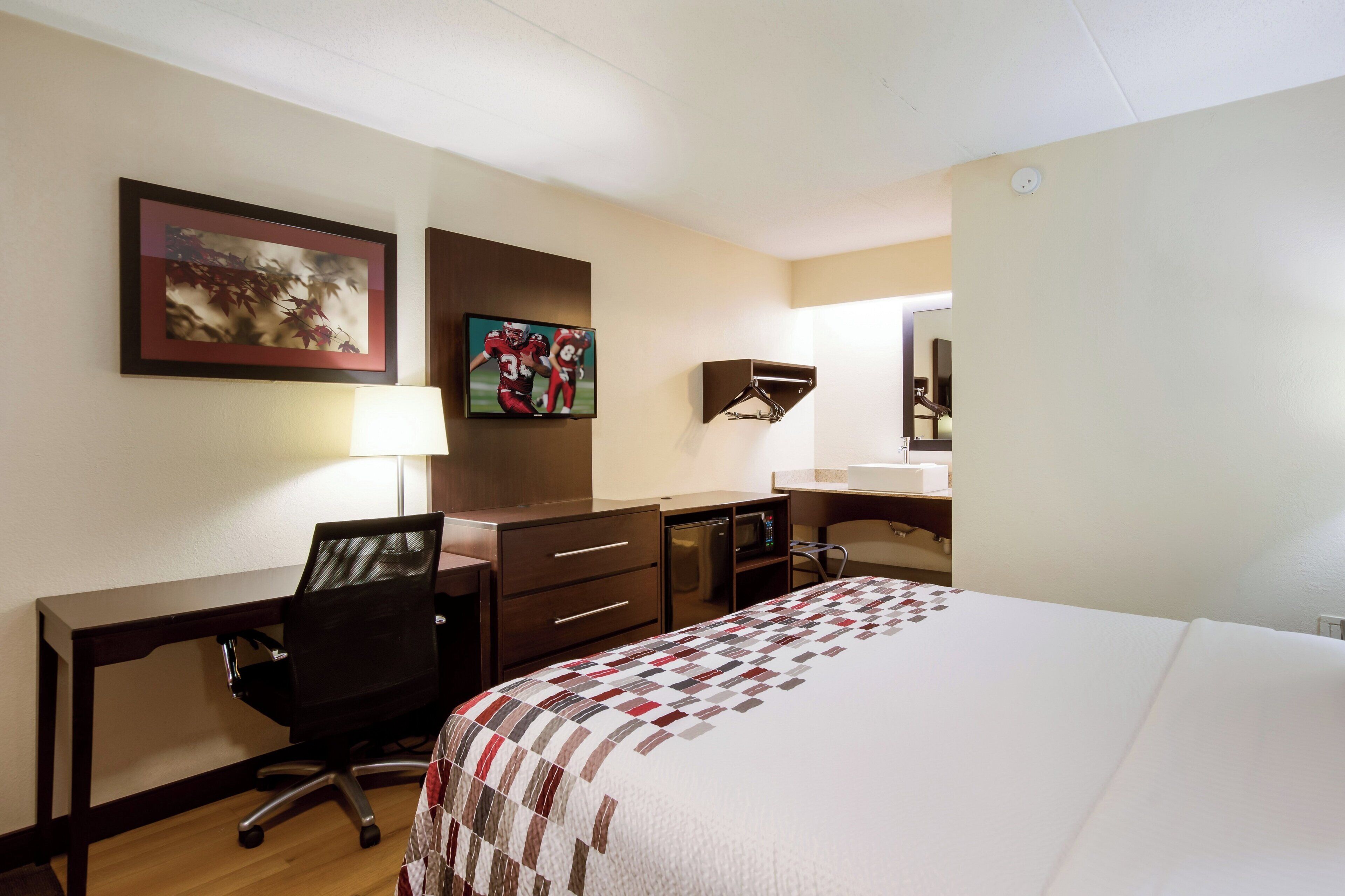 A hotel room with a bed, desk, chair, television, and a mirror.