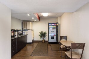Une chambre d’hôtel compacte comprenant un coin cuisine, un réfrigérateur, un espace repas avec une table et des chaises, ainsi qu’une petite plante en pot.