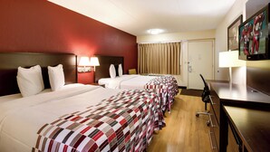 Een hotelkamer met drie bedden, een bureau, een televisie en een raam met gordijnen.