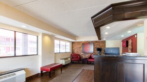 Een hotellobby met een receptiebalie, een zithoek en een uitzicht op de straat door grote ramen.
