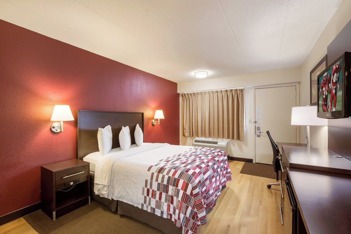 A hotel room with a bed, bedside lamps, a desk, and a television.