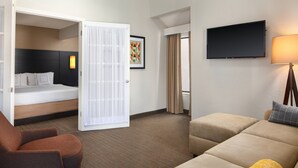 Une chambre d’hôtel avec un lit, un canapé, une chaise, une télévision et une lampe.
