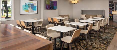 A modern dining area with multiple tables and chairs, a large wooden table, and a patterned carpet.