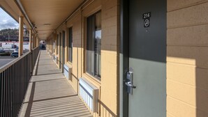 A corridor with a covered walkway, a door marked with the number 214, and a view of a parking area in the background.