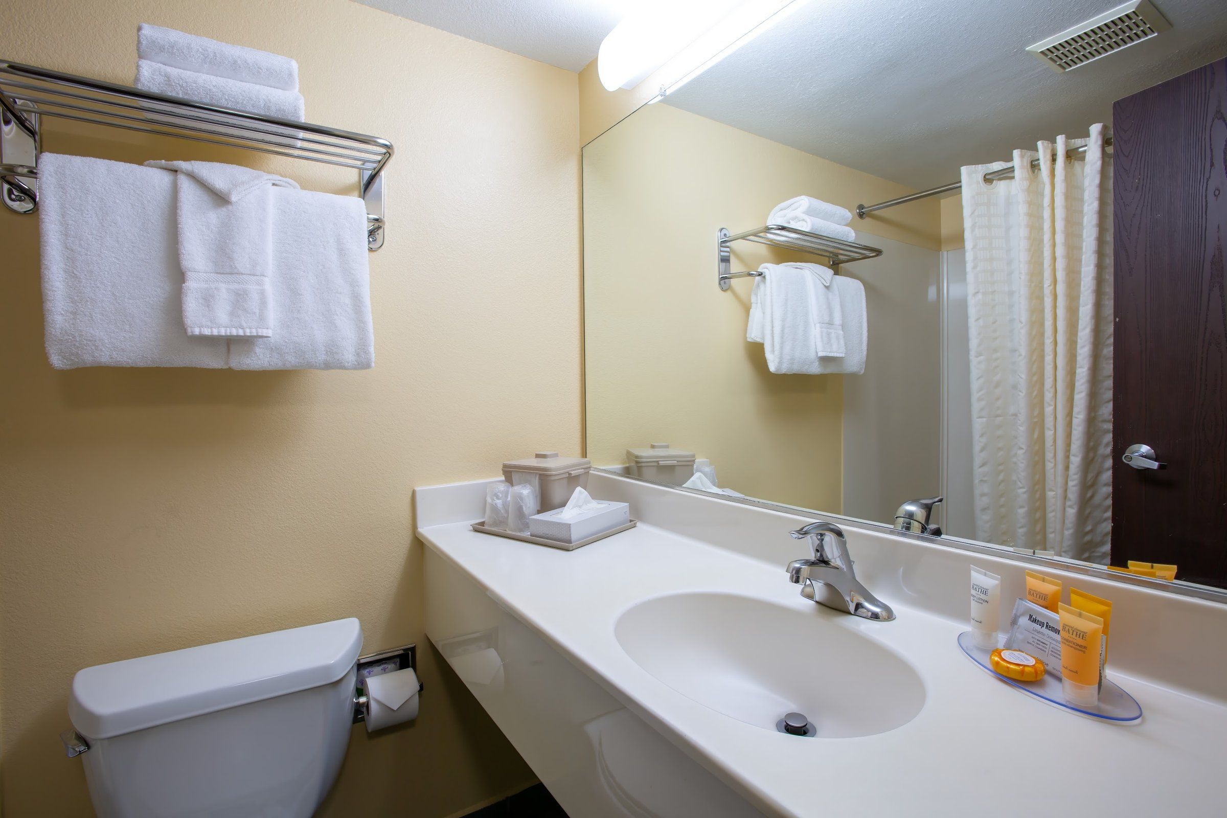 Un baño con inodoro, lavamanos, espejo y toallero.