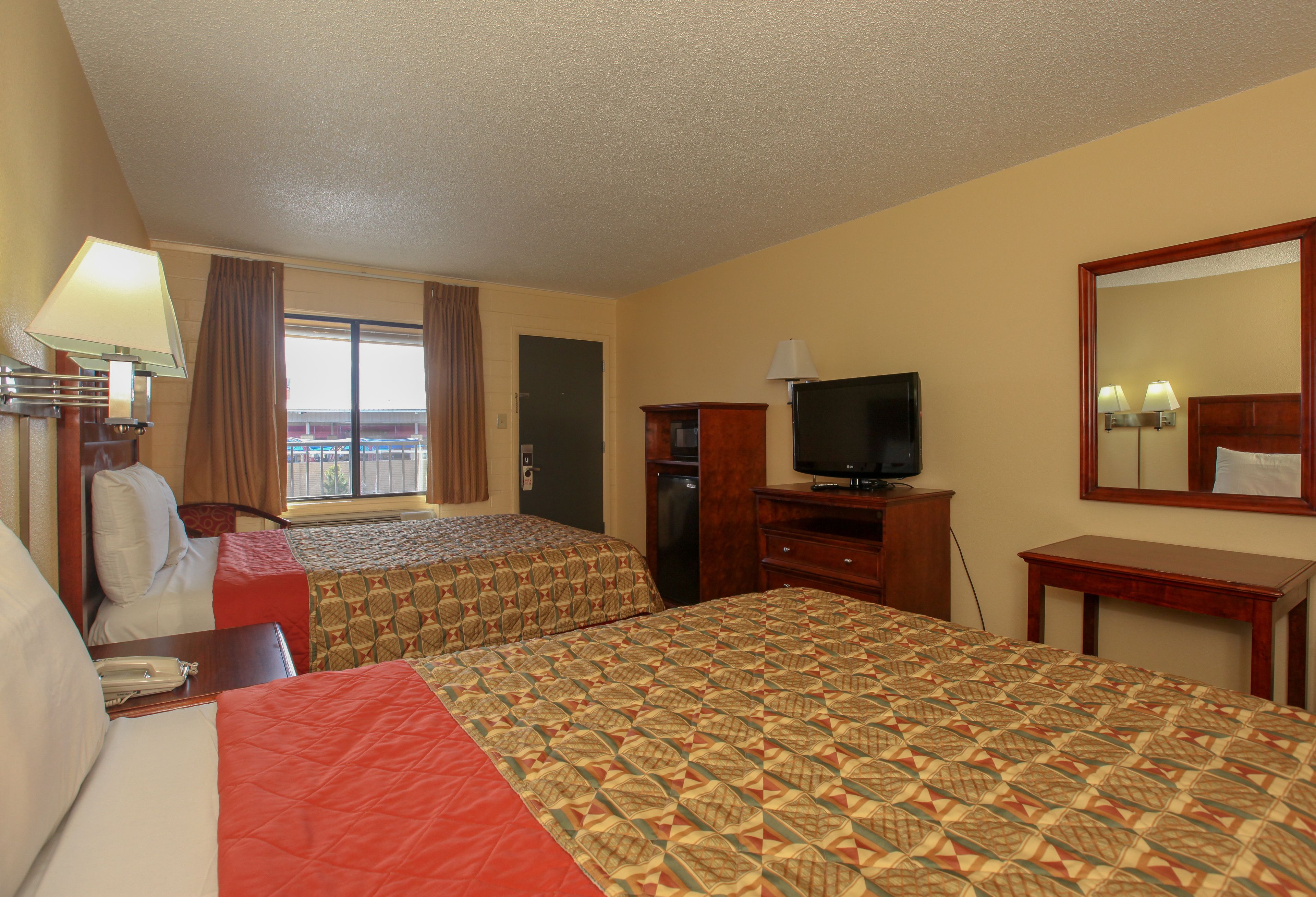 A hotel room with two beds, a television, a desk, and a window with curtains.