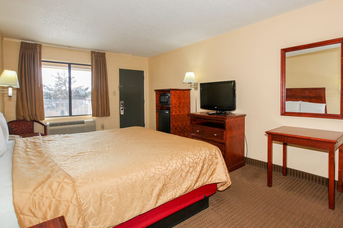 A hotel room with a bed, a television, a desk, a mirror, and a window with curtains.