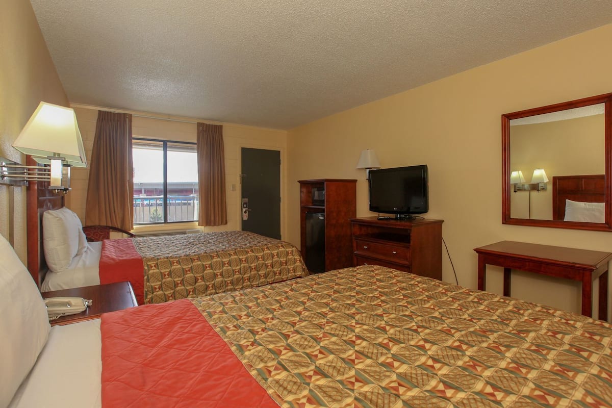 A hotel room with two beds, a television, a desk, a chair, a window with curtains, and a view of the outside.