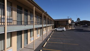 A hotel with a row of rooms, a parking lot, and a clear blue sky.