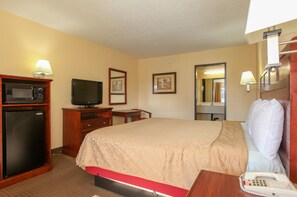 A hotel room with a bed, a television, a refrigerator, a desk with a telephone, and a mirror.