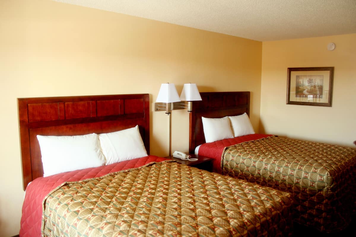 A hotel room with two single beds, each with a patterned bedspread and red headboard. There is a bedside table with a lamp and a telephone.