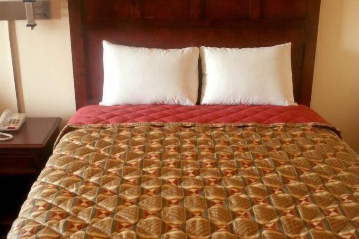 A neatly made bed with a patterned bedspread, a wooden headboard, and a bedside lamp.
