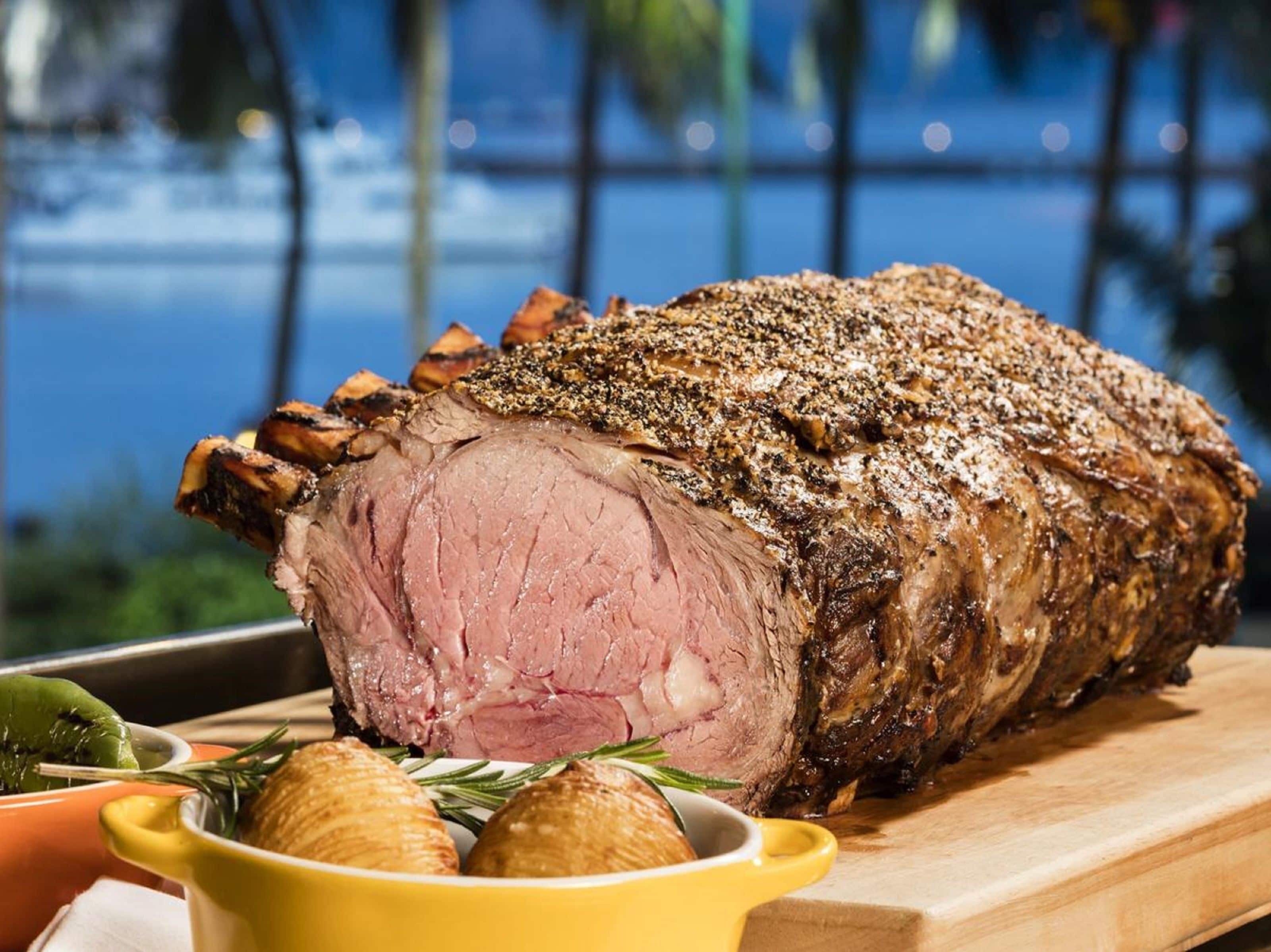 A roasted beef centerpiece with rosemary and garlic on a wooden board, set against a blurred outdoor background.