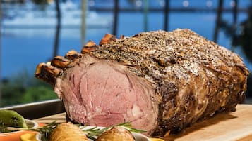 A roasted beef centerpiece with rosemary and garlic on a wooden board, set against a blurred outdoor background.