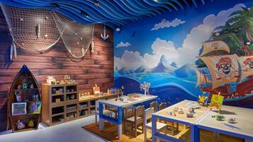 A children's playroom with wooden walls, a mural of a pirate ship, and various toys and art supplies.