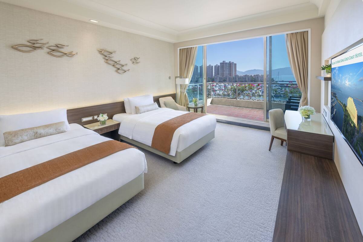 Une chambre d’hôtel avec deux lits, un bureau, une chaise et une grande fenêtre donnant sur la ville.