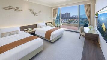 Quarto de hotel com duas camas, uma escrivaninha, uma cadeira e uma janela ampla com vista para a cidade.