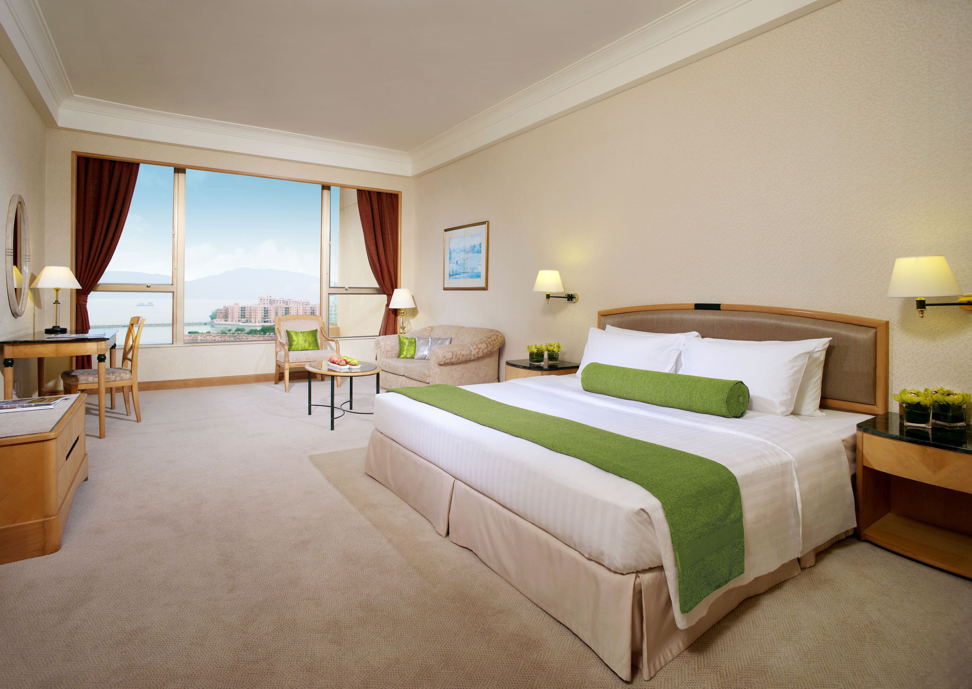 A hotel room with a large bed, a desk, a chair, and a view of the city.
