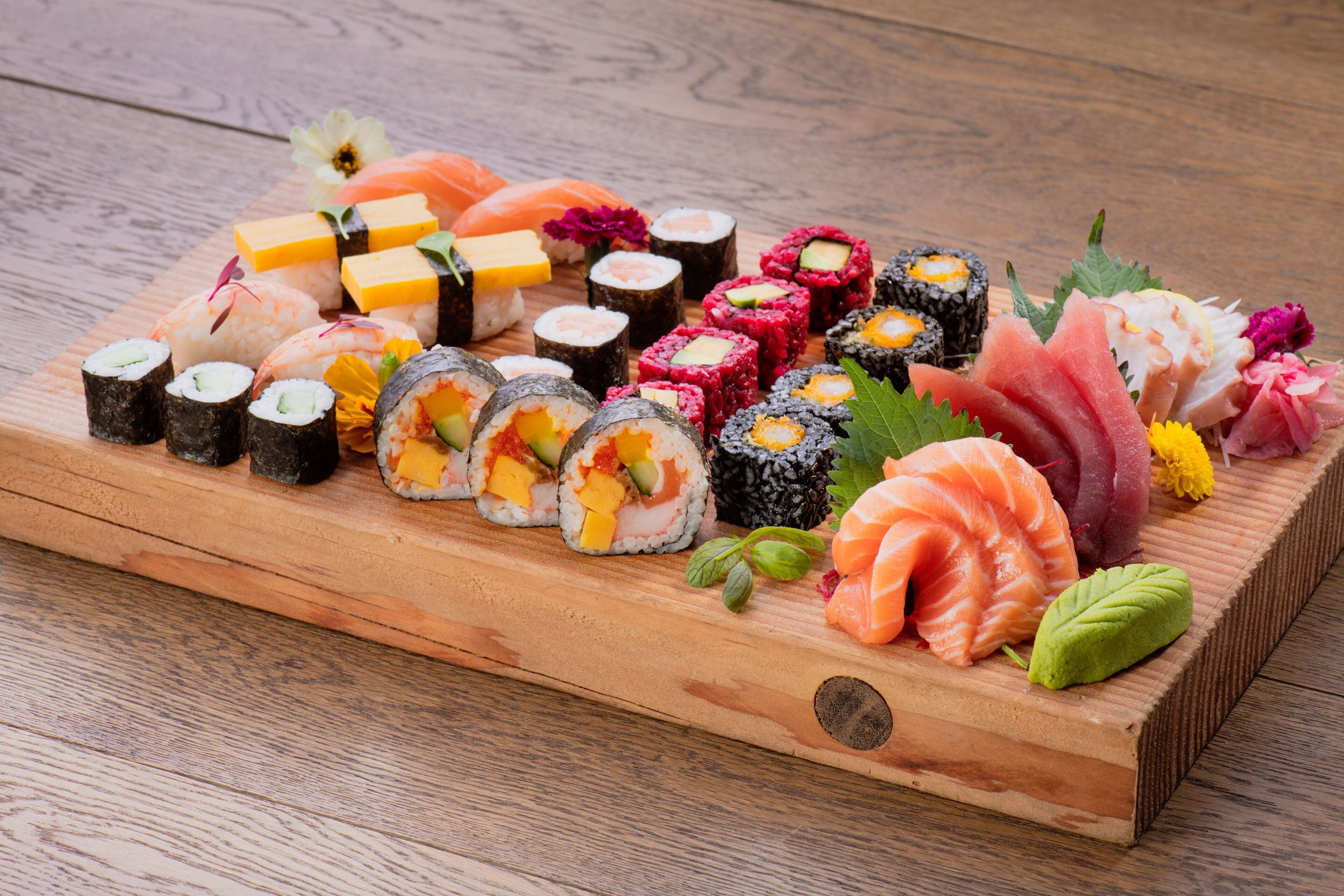 A wooden tray with various types of sushi and sashimi, including salmon and avocado rolls, arranged on a wooden table.