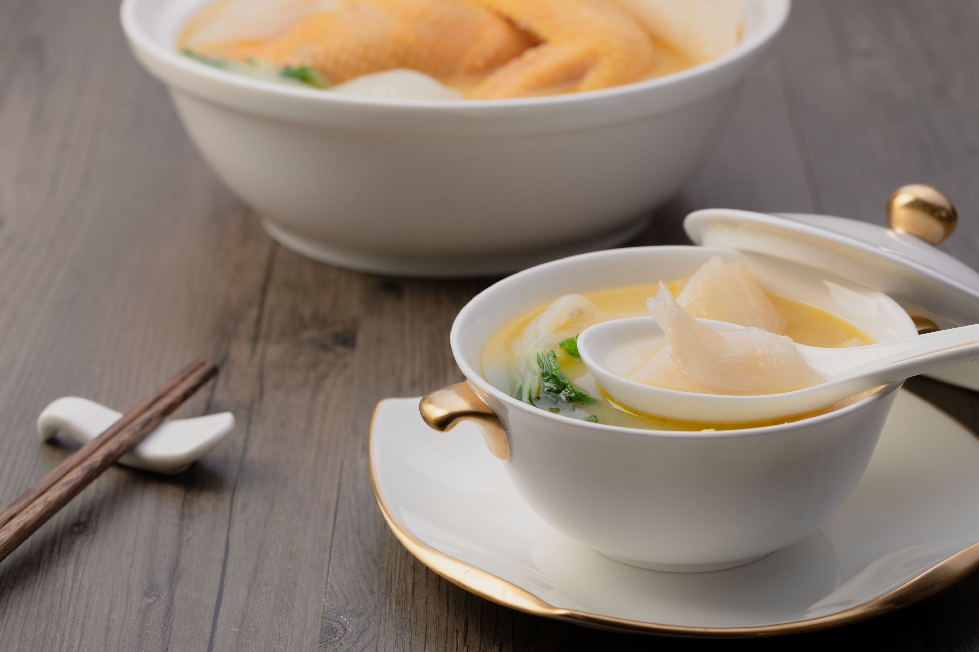 Un bol de soupe avec une cuillère, posé sur une assiette avec un bord doré.