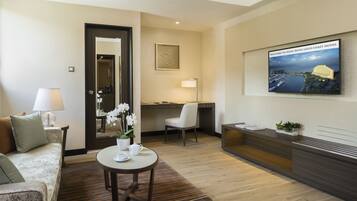 A hotel lobby with a reception desk, a seating area with a sofa and armchairs, a coffee table with a teapot, and a framed welcome sign.