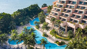 Een resort met meerdere zwembaden, palmbomen en een groot gebouw met balkons.