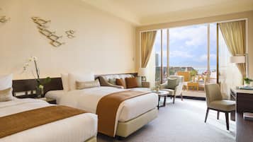 A hotel room with two beds, a desk, a chair, and a view of the city.