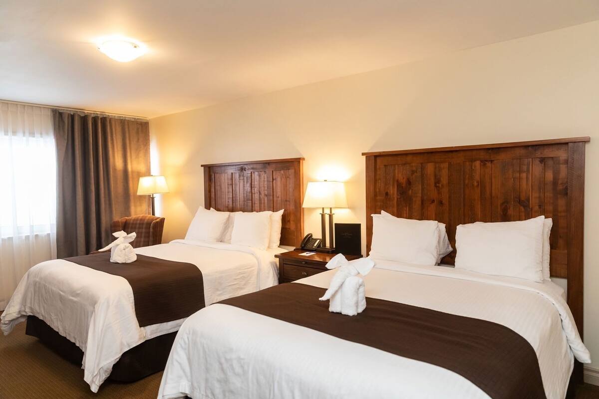 Habitación de hotel con dos camas, cabeceros de madera, lámparas de noche y una ventana con cortinas.