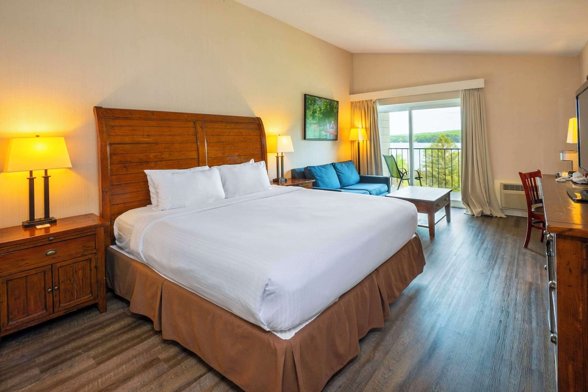 Una habitación de hotel con una cama grande, dos mesitas de noche con lámparas, un sofá, una mesita pequeña y una silla.