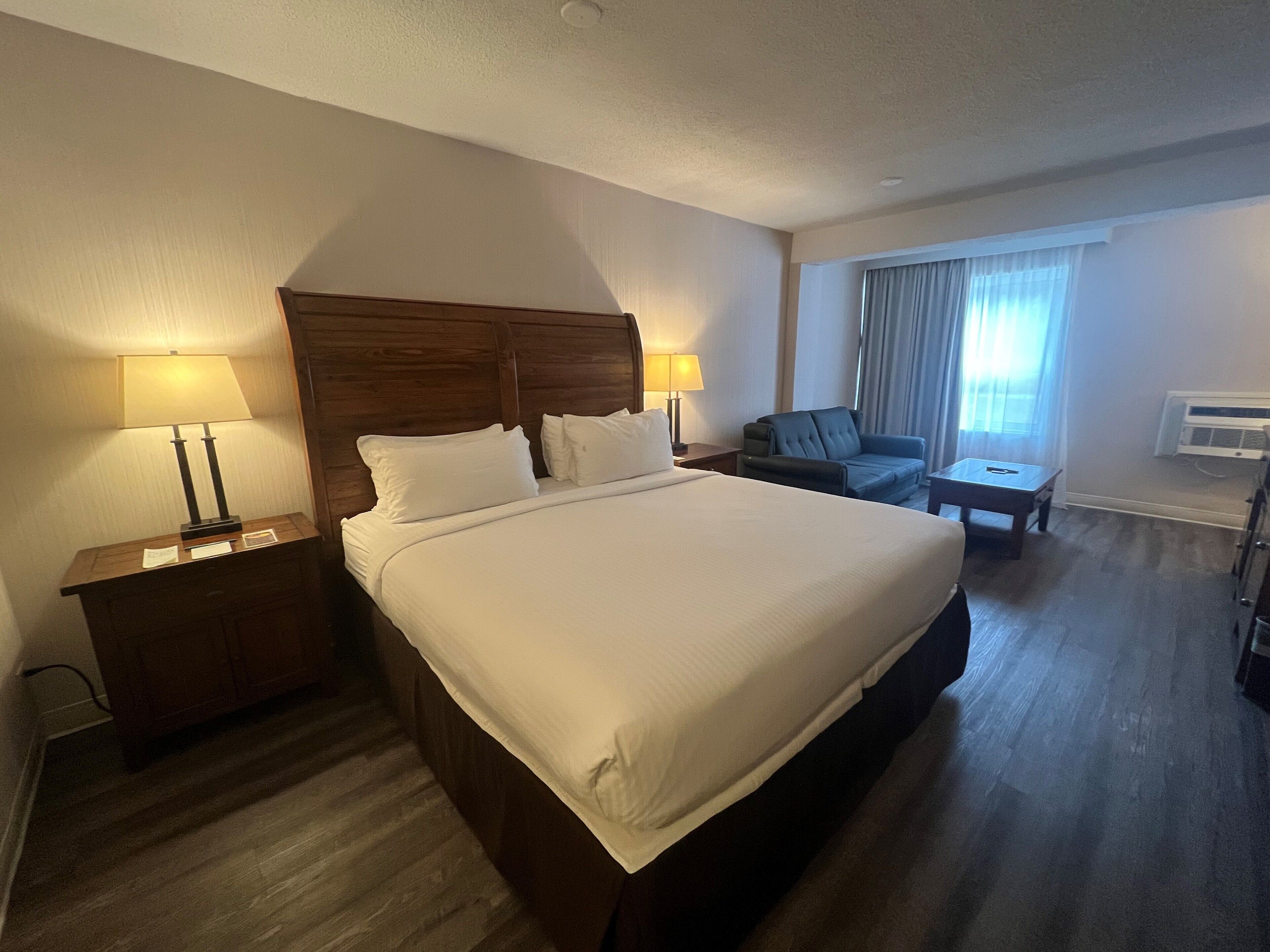Una habitación de hotel con una cama grande, dos mesitas de noche con lámparas, un sofá y un escritorio.