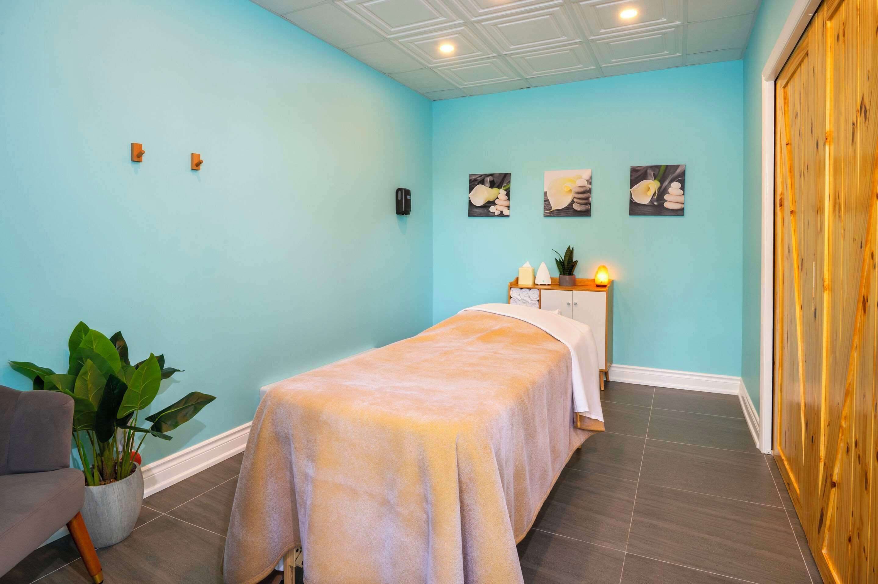 Une salle de spa équipée d’une table de massage, d’une plante en pot et d’œuvres d’art accrochées au mur.