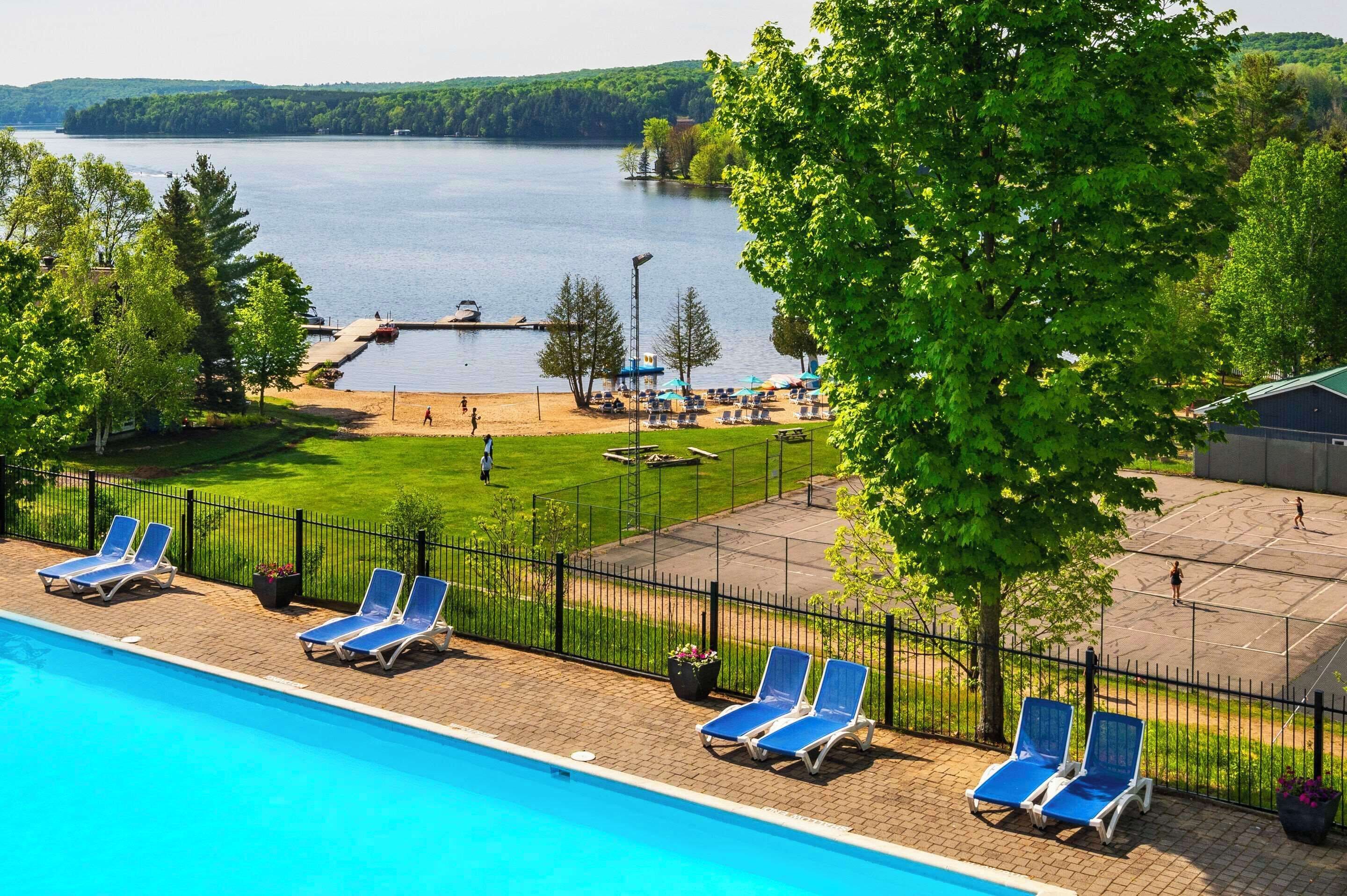 A swimming pool with lounge chairs, a tennis court, and a view of a lake.