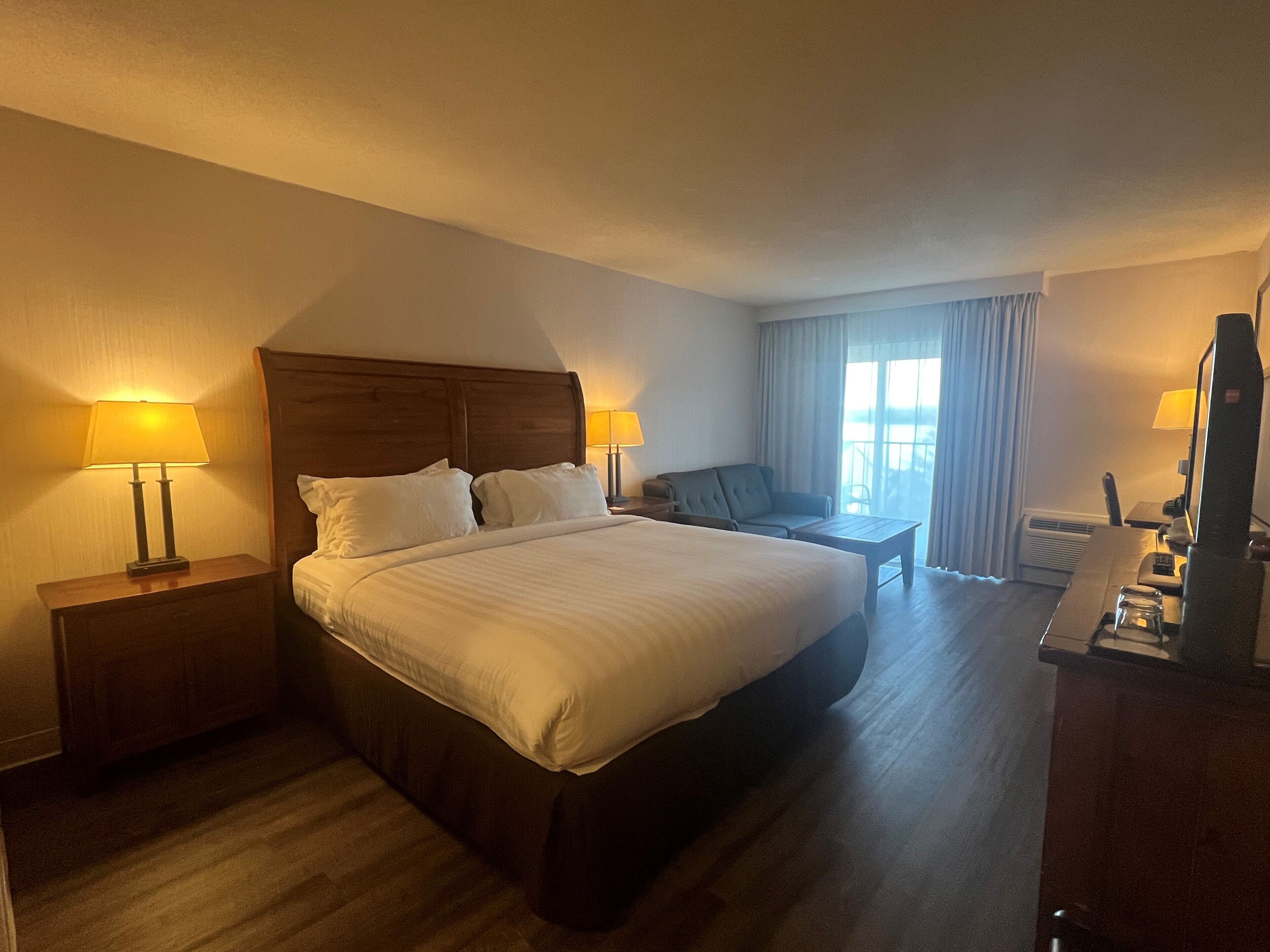 A hotel room with a large bed, two bedside tables with lamps, a desk with a chair, and a television.