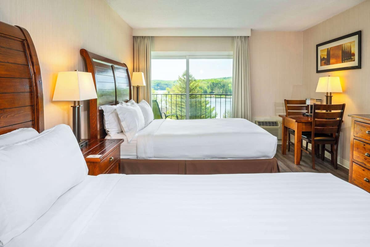 Habitación de hotel con dos camas, un escritorio, sillas y vista a un lago.