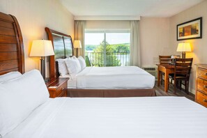 A hotel room with two beds, a desk, chairs, and a view of a lake.