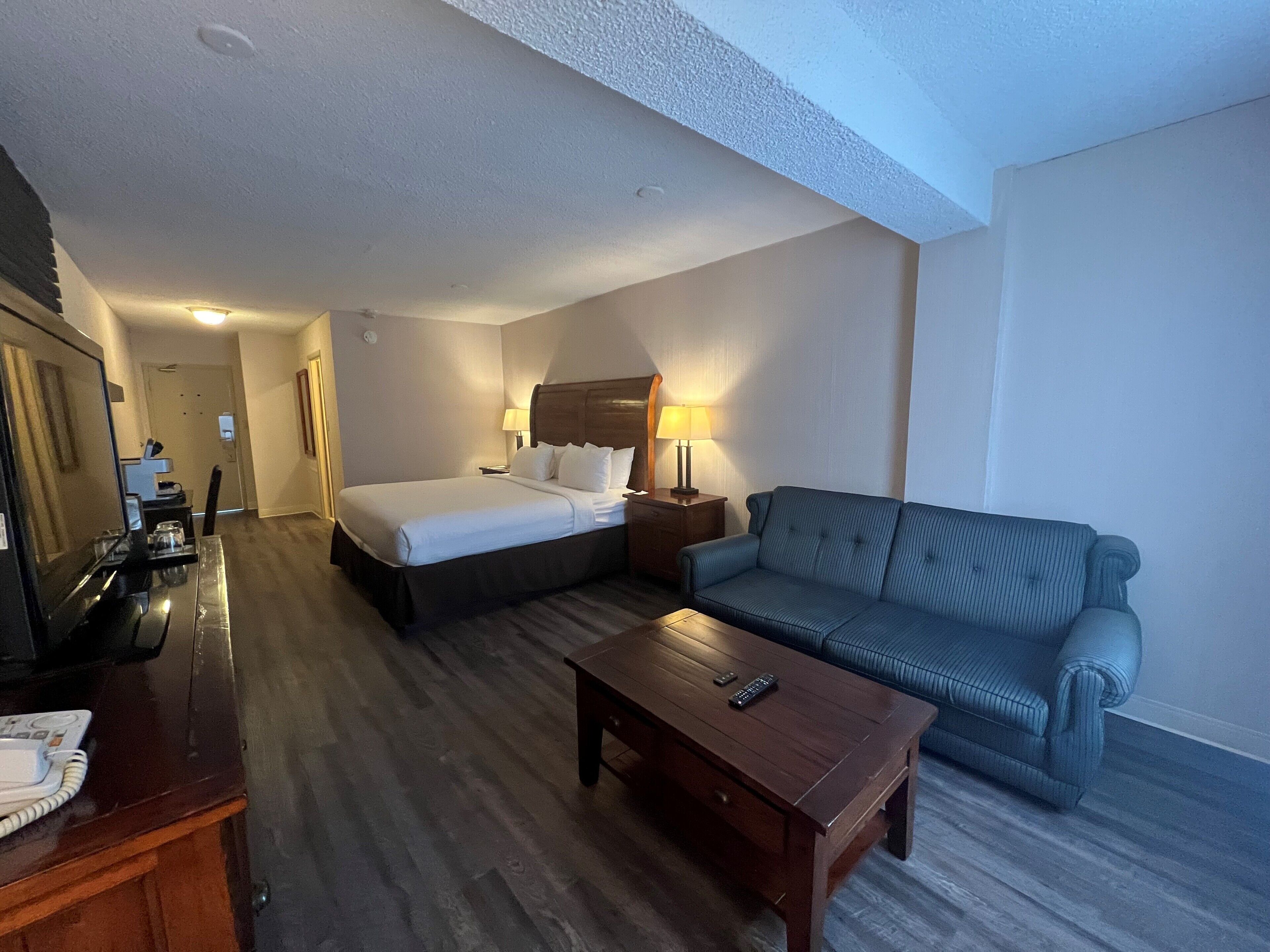 A hotel room with a bed, a sofa, a wooden coffee table, a desk with a telephone, and a lamp.