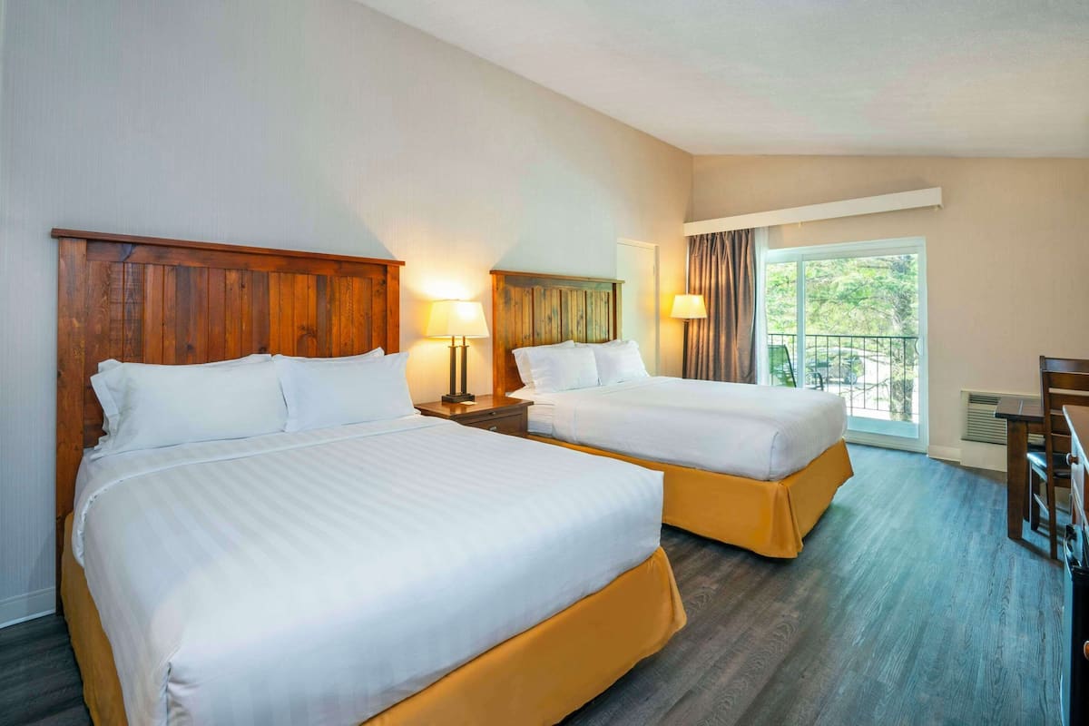 Habitación de hotel con dos camas, cabeceros de madera y un ventanal con vistas a zonas verdes.