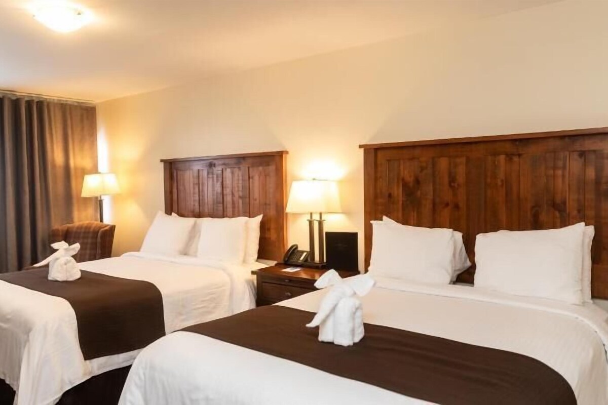 A hotel room with two beds, wooden headboards, bedside lamps, and a telephone on a nightstand.