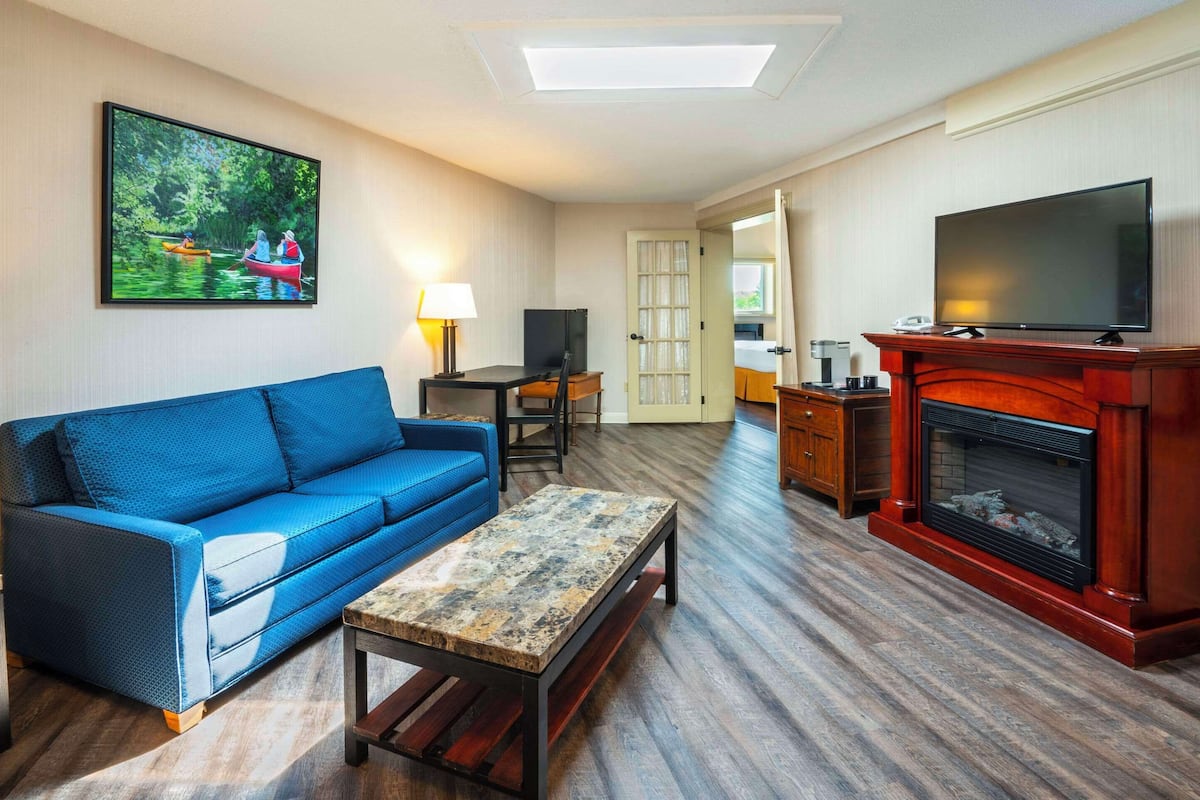 Una sala de estar con un sofá azul, una mesa de centro, una chimenea, un televisor y un cuadro de un paisaje fluvial.