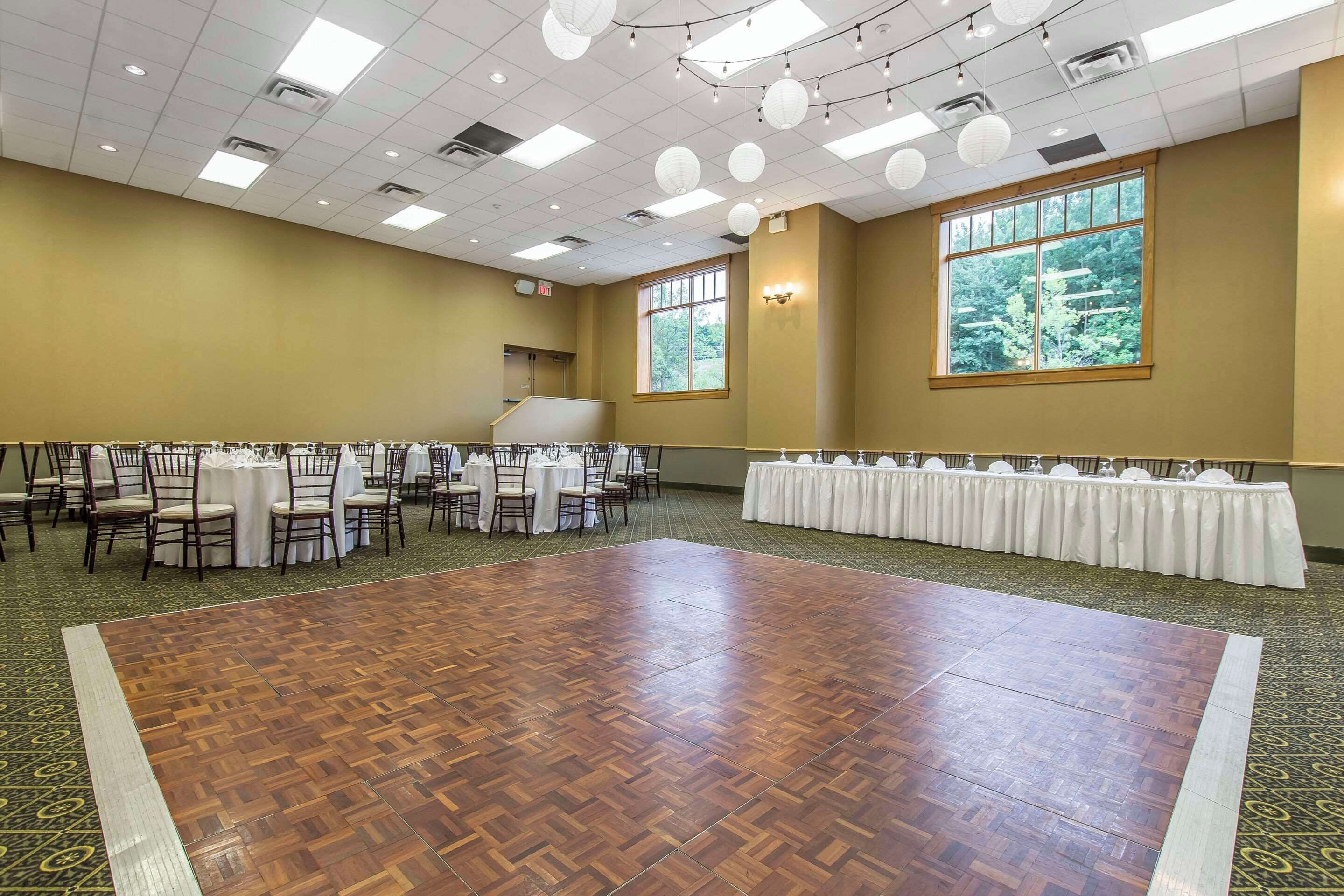 Un salón amplio con piso de madera, mesas con manteles blancos y sillas.