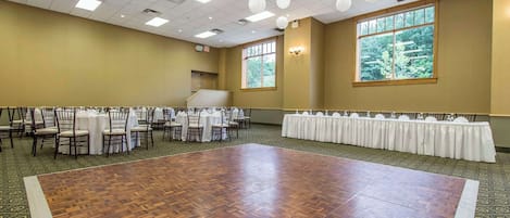 Un salón amplio con piso de madera, mesas con manteles blancos y sillas.