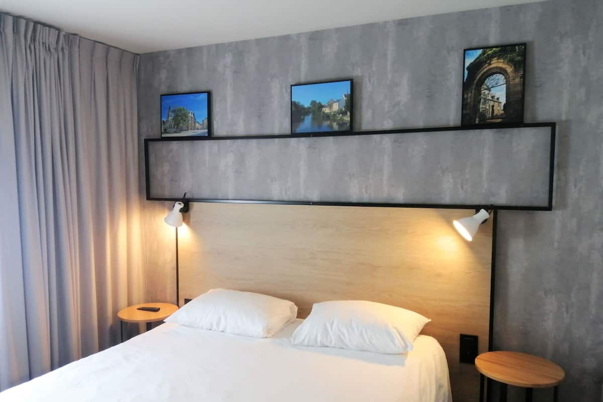 Ein Schlafzimmer mit einem Bett, zwei Nachttischlampen, einem Wandregal mit Bildern und einem runden Tisch.