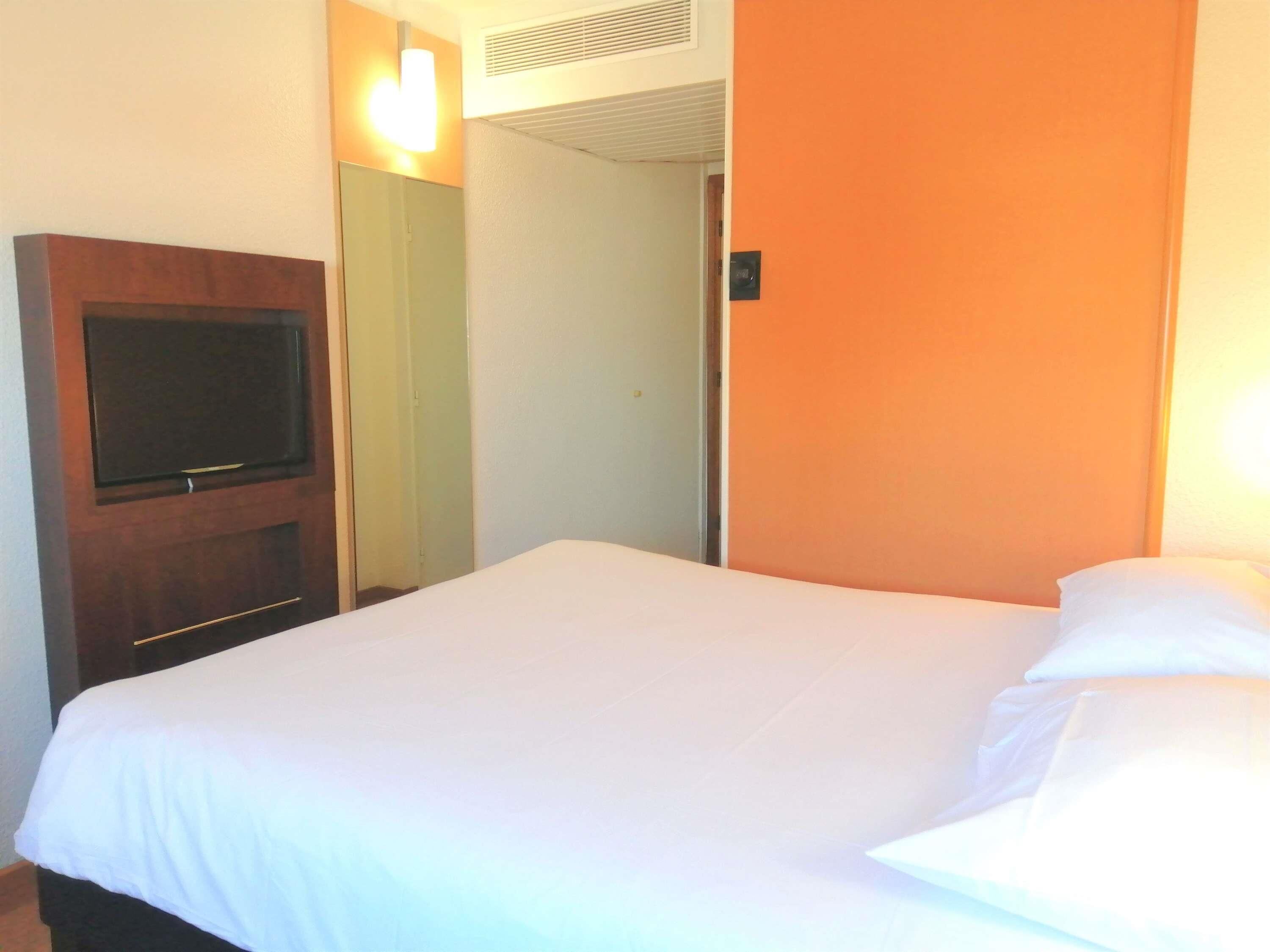 Habitación de hotel con cama, televisor en la pared y puerta que da a otra habitación.