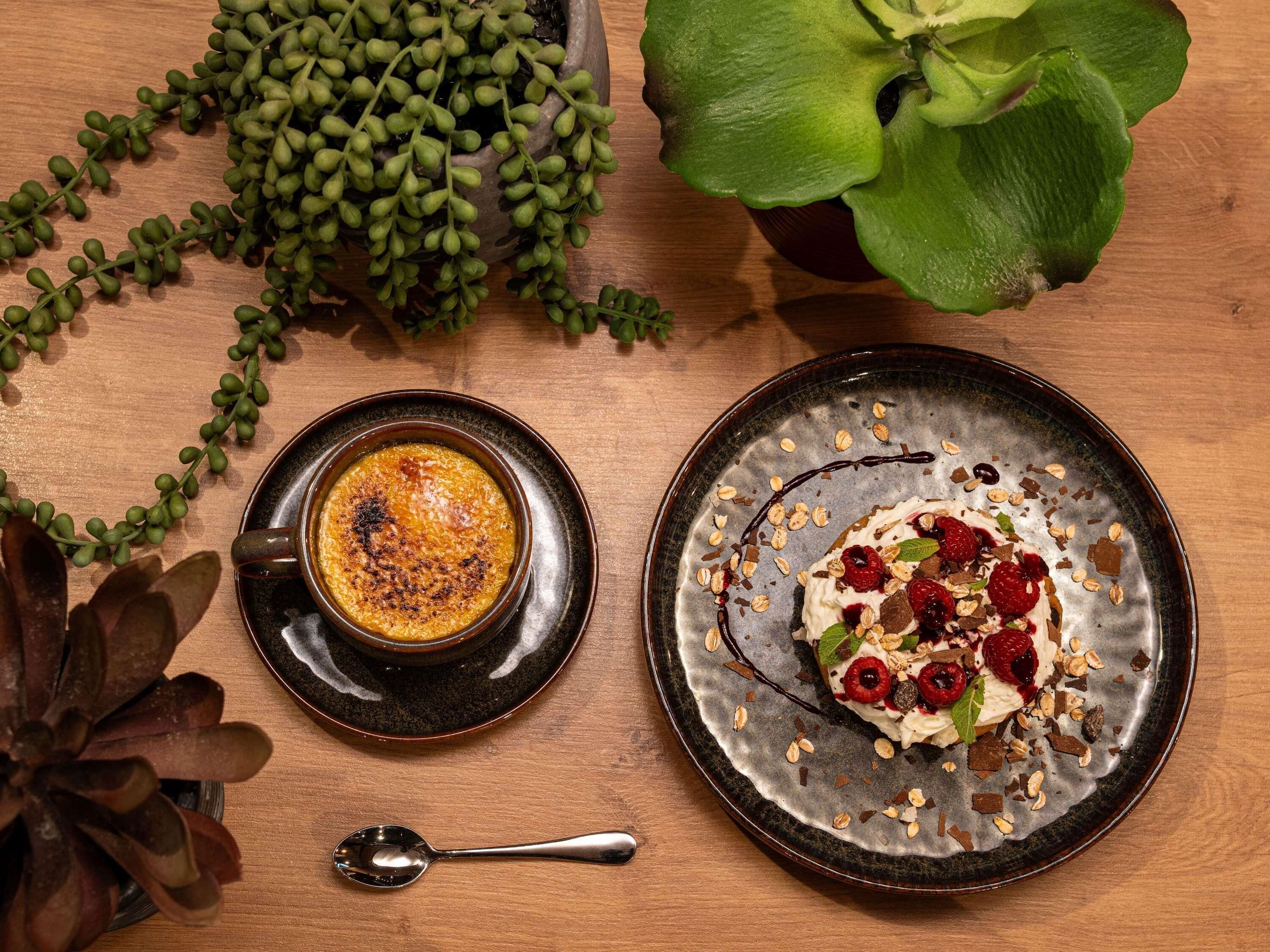 A dessert plate with fruit and nuts, a bowl of soup, and a potted plant on a wooden table.