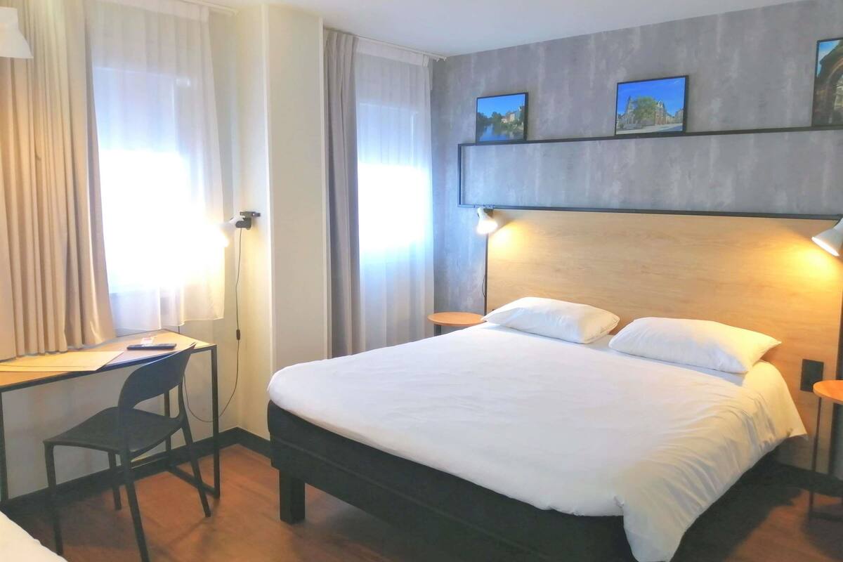 Une chambre d’hôtel avec un grand lit, un bureau avec une chaise et deux tables de chevet avec des lampes.