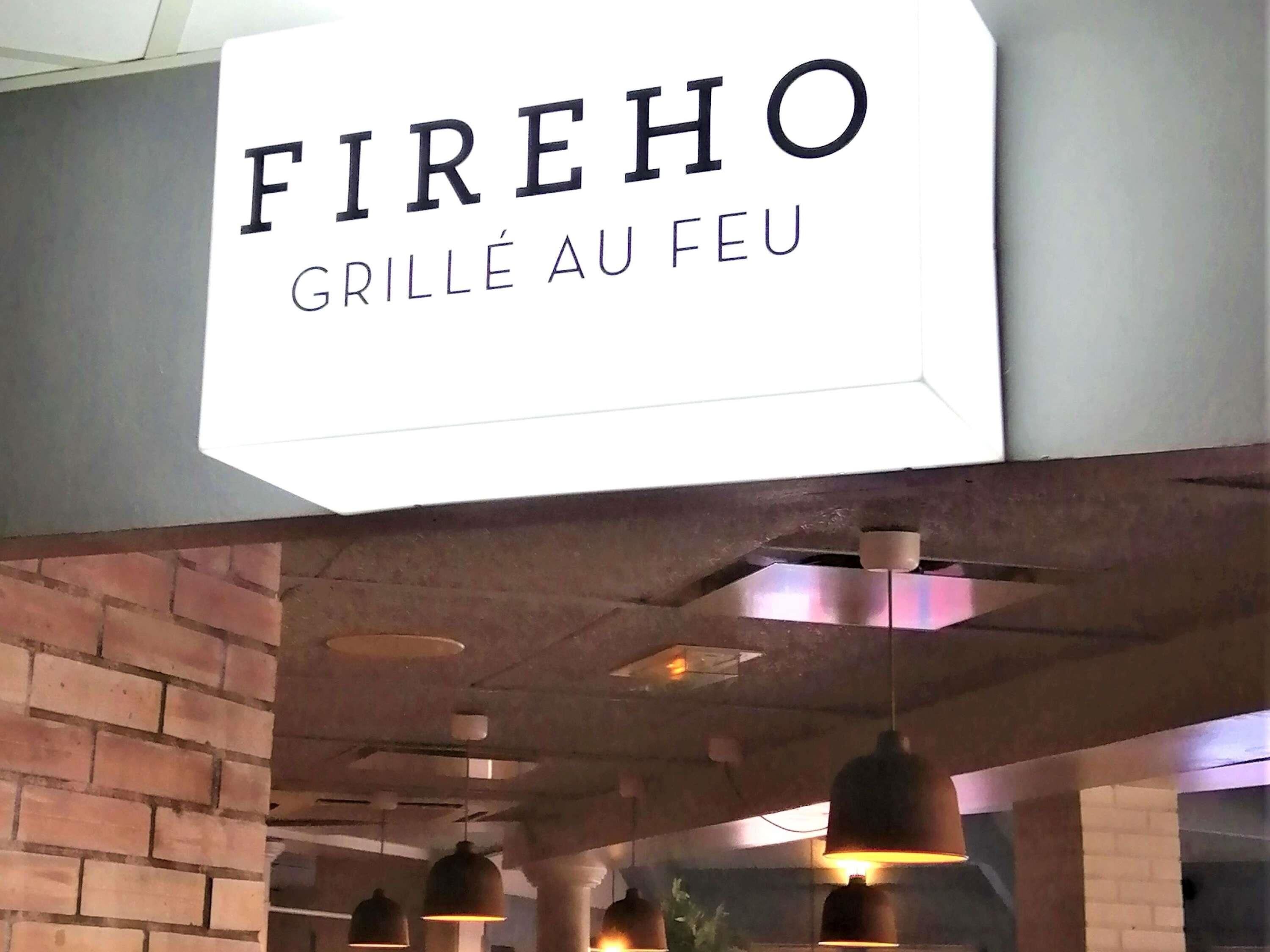 Un letrero que dice 'FIREHO GRILLÉ AU FEU', con un interior moderno que presenta ladrillo visto e iluminación colgante.
