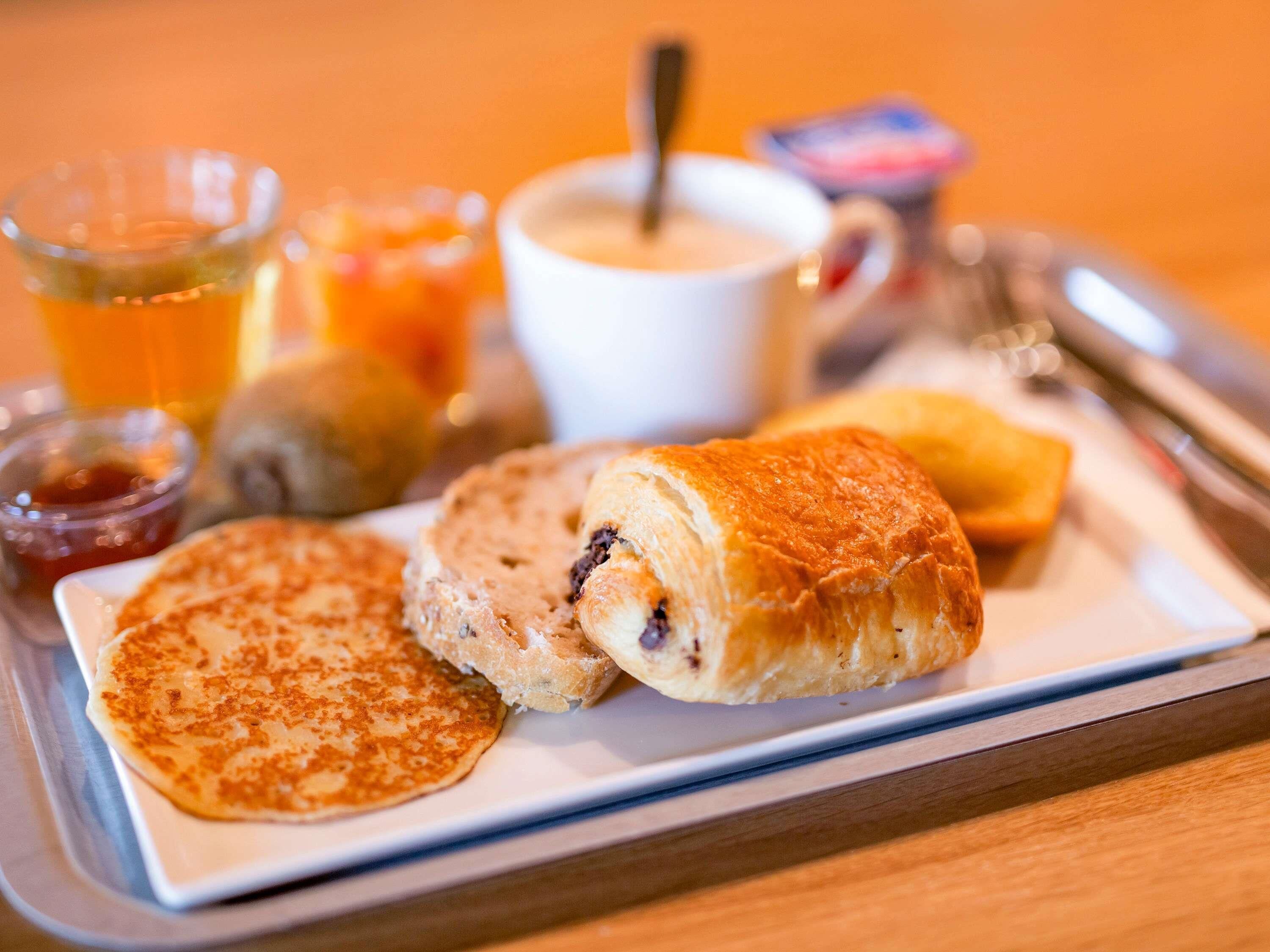A breakfast tray with pancakes, a croissant, and a beverage.