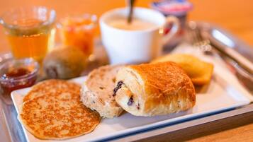 A breakfast tray with pancakes, a croissant, and a beverage.